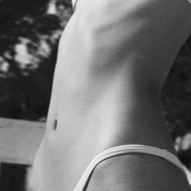 Primer plano en blanco y negro del torso tonificado de una persona (desde las costillas hasta la cadera) usando la parte inferior de un bikini blanco. Detox Body Wash | Activated Charcoal and Green Tea