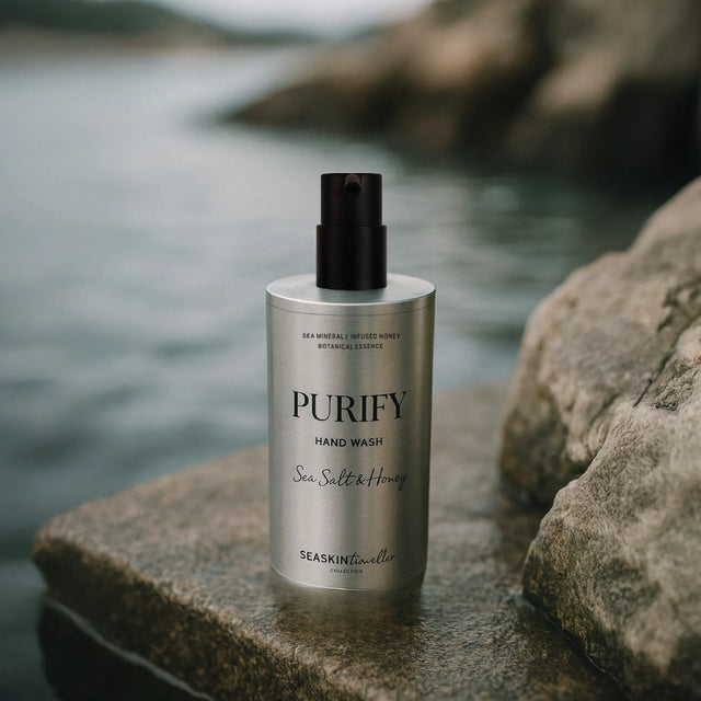 Jabón facial hidratante de Seaskin, 100% orgánico y artesanal, con Miel, Aceites y Propóleos sobre una piedra y fondo beige Botella de aluminio de limpiador de manos 'Purify Sea Salt & Honey' con dispensador negro, sobre roca natural mojada junto a agua corriente.