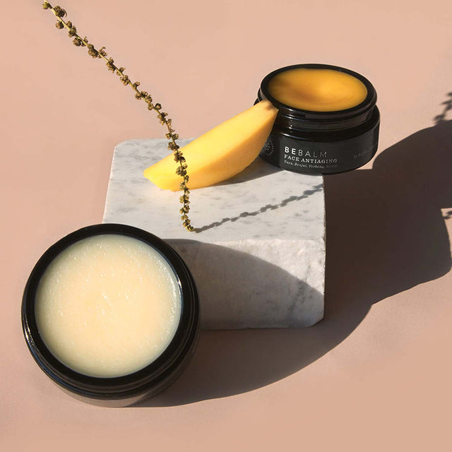 Bálsamos faciales sobre mármol, con una rodaja de mango, destacando la pureza y nutrición de los productos Bálsamos faciales sobre mármol, con una rodaja de mango, destacando la pureza y nutrición de los productos