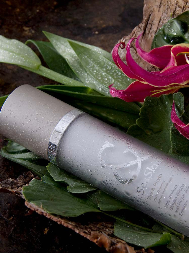 Frasco de cosmético SeaSkin sobre hojas húmedas y flores, representando frescura y pureza natural. Frasco de cosmético SeaSkin sobre hojas húmedas y flores, representando frescura y pureza natural.