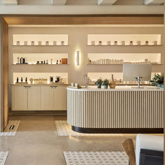 Recepción de spa moderna con mostrador de madera curvo, estanterías con productos de cuidado personal iluminadas y decoración minimalista en tonos cálidos Recepción de spa moderna con mostrador de madera curvo, estanterías con productos de cuidado personal iluminadas y decoración minimalista en tonos cálidos