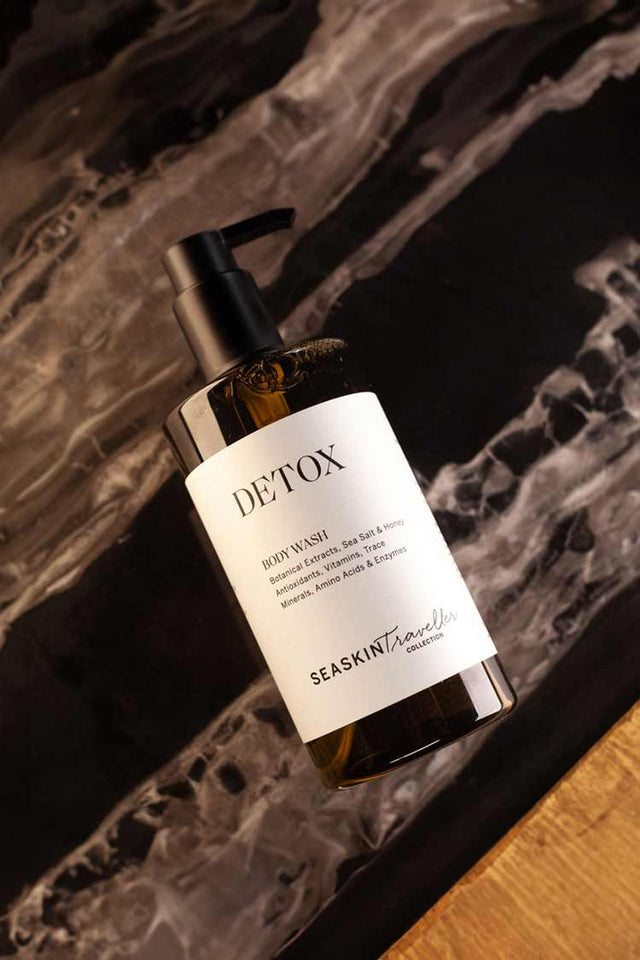 Botella de gel corporal detox en envase ámbar sobre fondo de mármol negro vetado.