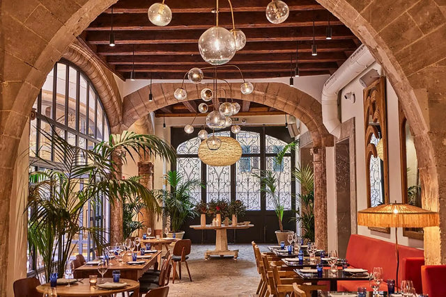 Restaurante elegante con arcos de piedra, techo de vigas de madera, mesas puestas y plantas decorativas en Palma de Mallorca. Restaurante elegante con arcos de piedra, techo de vigas de madera, mesas puestas y plantas decorativas en Palma de Mallorca.