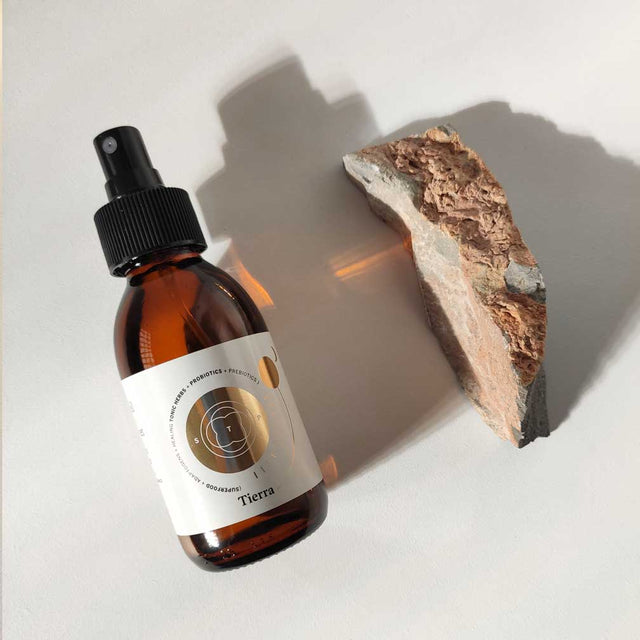 Envase de aceite corporal antioxidante de Smell The Planet, 100% orgánico con propiedades antioxidantes, circulatorias e hidratantes sobre superficie blanca al lado de piedra