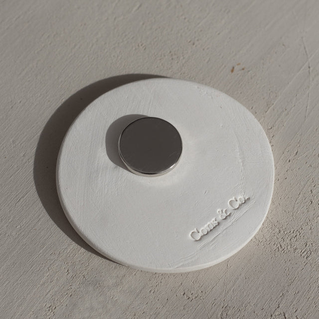 Parte trasera de imán de barro redondo color blanco con sello de la marca Cons & Co Parte trasera de imán de barro redondo color blanco con sello de la marca Cons & Co