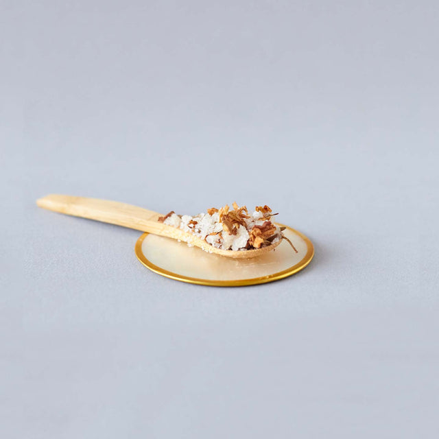 Cuchara de madera con sales de baño de Beseaskin, 100% orgánicas a base de Geranio, Bergamota, Rosa, Lavanda y Jazmín con fondo gris.