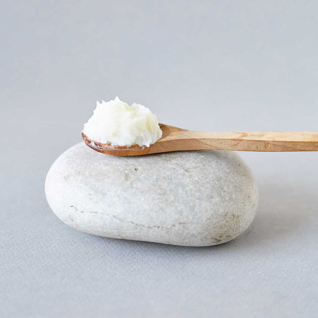 Cuchara de palo con bálsamo exfoliante corporal antiaging de Beseaskin, 100% orgánico a base de Lavanda y Palo de Rosa sobre piedra con fondo gris.