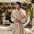 Mujer con albornoz de algodón certificado 100% orgánico en color beige de Seaskin Life, en una terraza con hamacas y plantas de fondo.