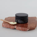 Bálsamo limpiador facial Bebalm con aplicador de madera sobre piedra roja.