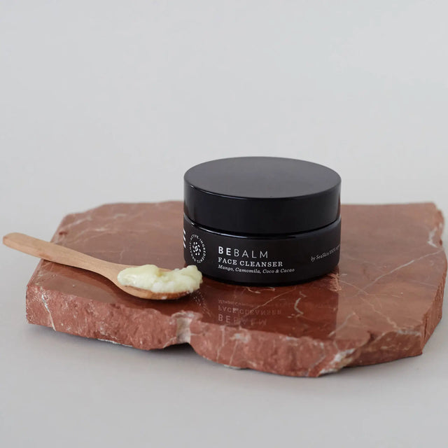 Bálsamo limpiador facial Bebalm con aplicador de madera sobre piedra roja.