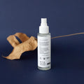 Envase de bruma floral facial iluminadora de Beseaskin, 100% orgánica a base de Rosa, Agua Termal y Concentrado de Posidonia con fondo azul oscuro y una hoja.