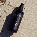 Envase de aceite corporal bronceador de Beseaskin, 100% orgánico a base de Raw Cacao y Coco en una mano dentro del mar.