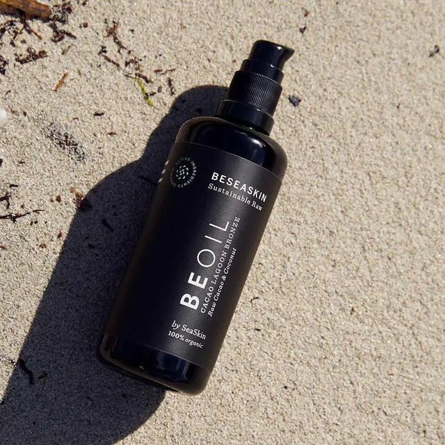 Envase de aceite corporal bronceador de Beseaskin, 100% orgánico a base de Raw Cacao y Coco en una mano dentro del mar.
