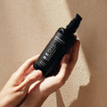 Envase de aceite corporal relajante de Beseaskin, 100% orgánico a base de Sándalo y Naranja en unas manos con fondo beige.