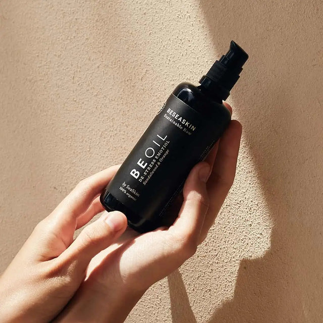 Envase de aceite corporal relajante de Beseaskin, 100% orgánico a base de Sándalo y Naranja en unas manos con fondo beige.