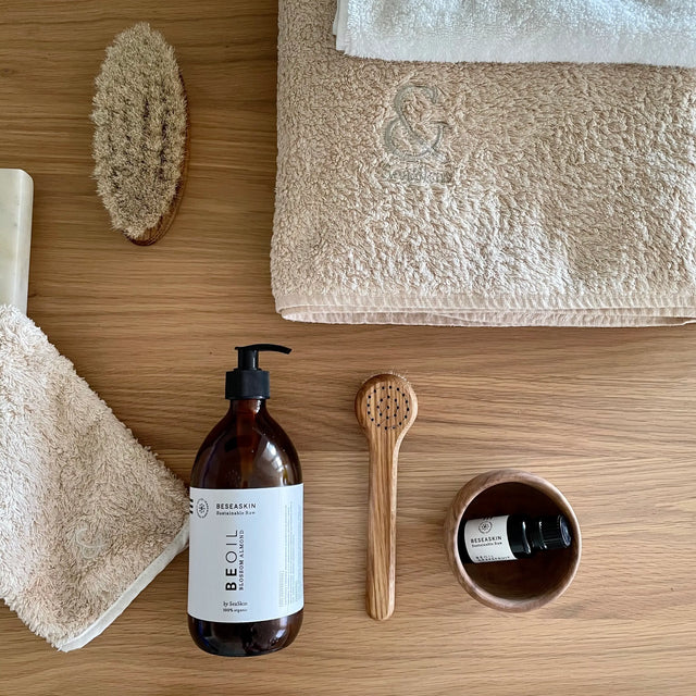Mesa de madera con Cepillo Corporal y Cepillo Facial de SeaSkin Life, 100% orgánicos, a su lado, dos productos beoil de Beseaskin, un cuenco de madera y toallas de SeaSkin Life.
