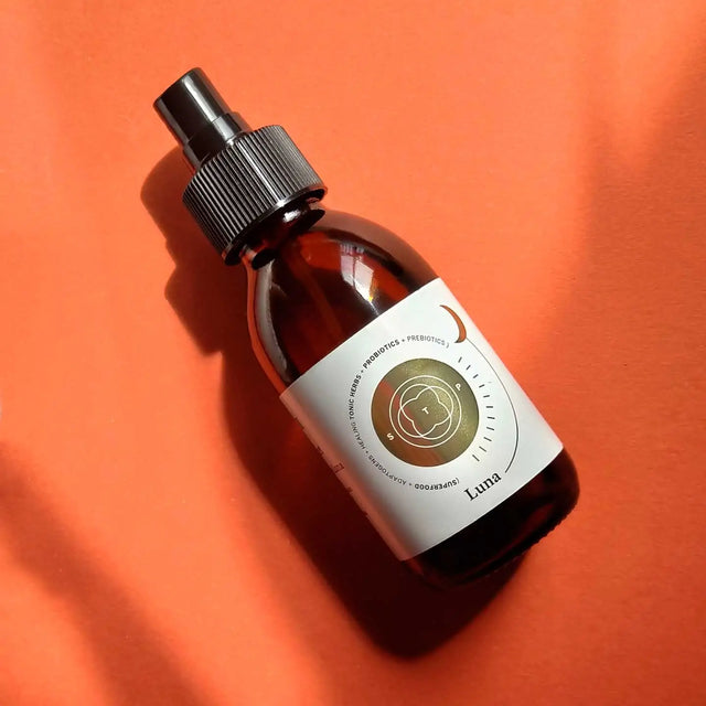 Envase de aceite corporal regenerador de Smell The Planet, 100% orgánico con propiedades antioxidantes e hidratantes obre superficie naranja.
