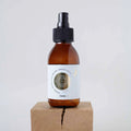 Elixir Luna en botella de spray de vidrio ámbar con etiqueta dorada, colocado sobre un bloque de madera natural.