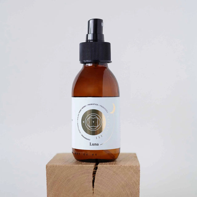 Elixir Luna en botella de spray de vidrio ámbar con etiqueta dorada, colocado sobre un bloque de madera natural.
