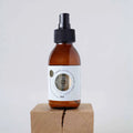 Elixir Sol en botella de spray de vidrio ámbar con etiqueta dorada, colocado sobre un bloque de madera natural.