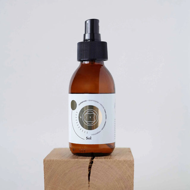 Elixir Sol en botella de spray de vidrio ámbar con etiqueta dorada, colocado sobre un bloque de madera natural.