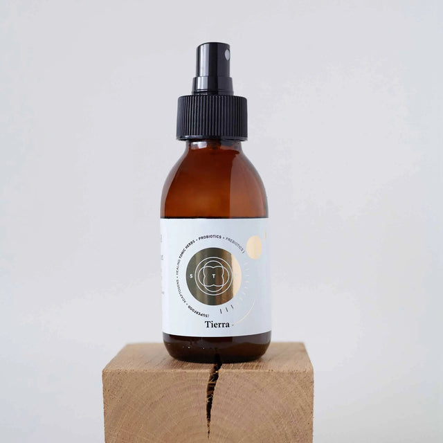 Elixir Tierra en botella de spray de vidrio ámbar con etiqueta dorada, colocado sobre un bloque de madera natural.