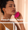 Retrato de una mujer con cabello rizado y tez morena, sosteniendo el dispositivo de tonificación facial FOREO BEAR™ 2 de color fucsia brillante cerca de su mejilla. El texto promocional dice: 'BEAR™ 2 Resultados reales'.