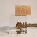 Jabón facial hidratante de Seaskin, 100% orgánico y artesanal, con Miel, Aceites y Propóleos sobre mesa de mármol con flores.