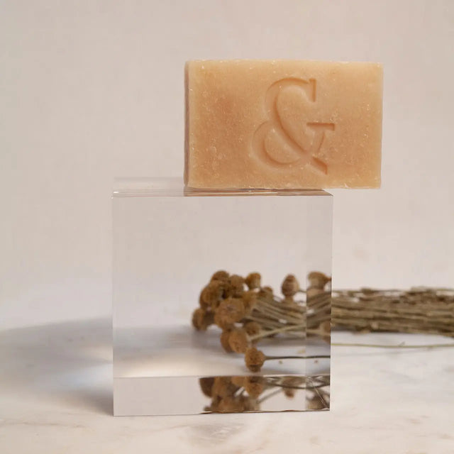 Jabón facial hidratante de Seaskin, 100% orgánico y artesanal, con Miel, Aceites y Propóleos sobre mesa de mármol con flores.