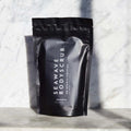 Envase de bálsamo exfoliante corporal nutritivo de Beseaskin, 100% orgánico a base de Sándalo y Naranja con fondo de mármol.