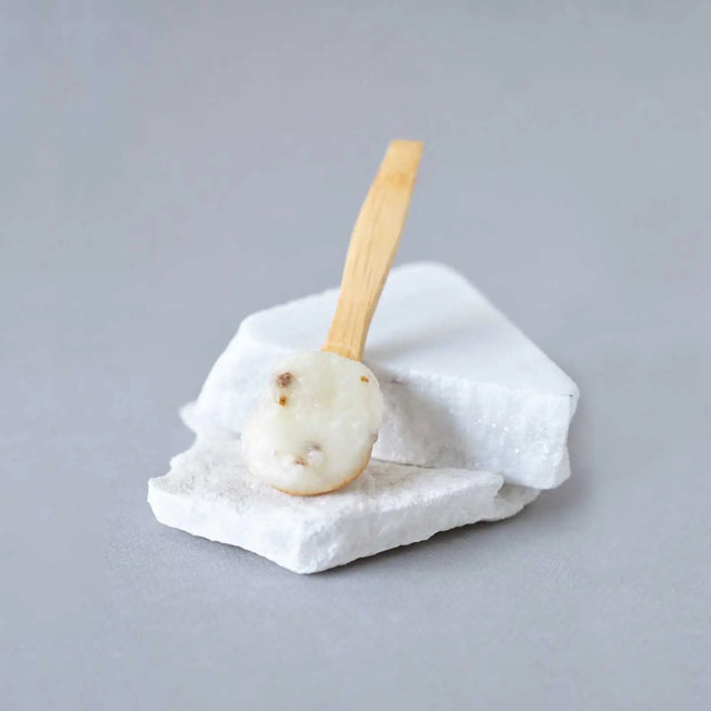 Cuchara de madera con bálsamo exfoliante corporal circulatorio de Beseaskin, 100% orgánico a base de Lemongrass y Geranio sobre piedra blanca con fondo gris.