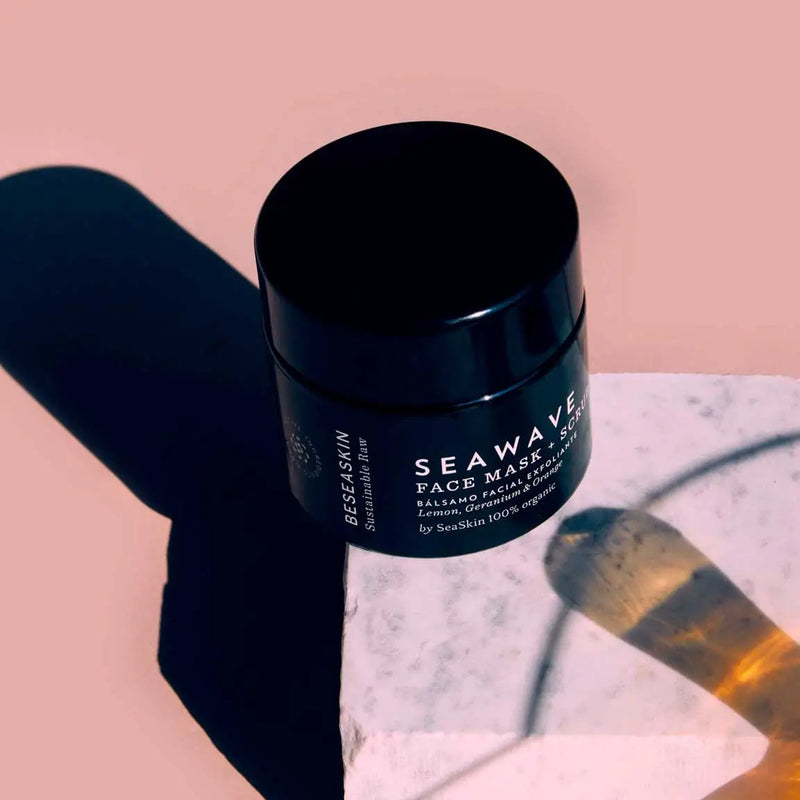 Envase de bálsamo facial exfoliante de Beseaskin, 100% orgánico con Limón, Geranio y Naranja sobre piedra con un fondo rosa.