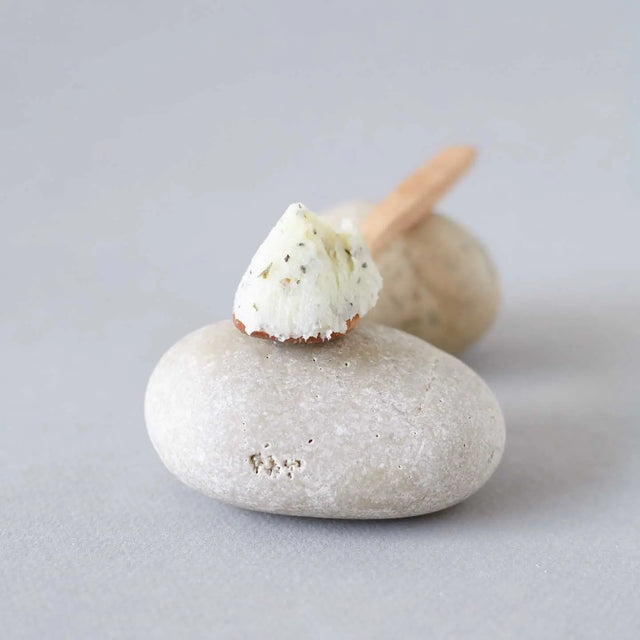 Cucara de madera con bálsamo exfoliante corporal tonificante de Beseaskin, 100% orgánico a base de Menta y Tomillo sobre piedras con fondo gris.
