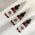 Envases de los elixires corporales Luna, Sol y Tierra de Smell The Planet, 100% orgánicos con hierbas tónicas curativas y probióticos, sobre superficie blanca.