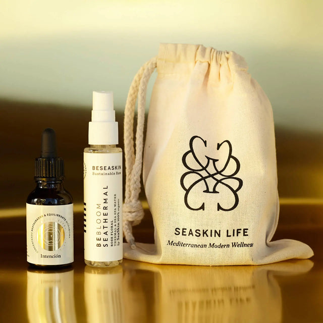 Envases de Elixir Intención (Skinbooster) y Bebloom Seathermal Rose (iluminador) con bolsa de tela de Seaskin Life sobre superficie dorada.