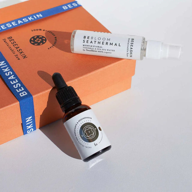 Envases de bruma floral facial de Mirto reafirmante y aceite facial Ío hidratante y regenerador, 100% orgánicos sobre caja de Beseaskin en superficie gris.