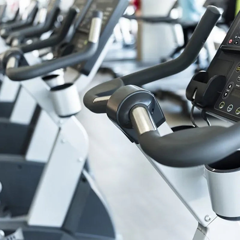 Primer plano de bicicletas estáticas en fila dentro del gimnasio del Club de Mar en Palma de Mallorca, con pantallas digitales y manillares ergonómicos.