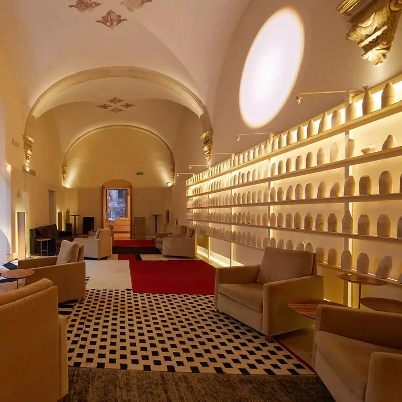 Espacio interior elegante con techos abovedados, sillones tapizados y una pared iluminada con estanterías llenas de esculturas blancas, en un ambiente artístico y sofisticado.