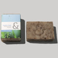 Pastilla de jabón artesanal de color marrón claro, con el relieve de un signo de 'ampersand' (&) en el centro, junto a su caja de cartón de color azul y verde con el texto 'SeaSkin Soap Mediterranean Essence Handmade Soap'.
