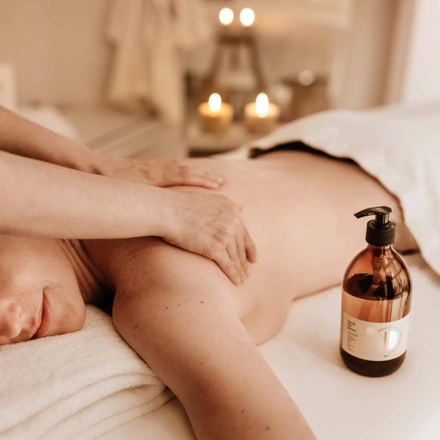Masaje de espalda y hombros en un spa con aceite, velas y luz cálida, representando un tratamiento corporal holístico y relajante.