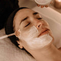 Aplicación de una mascarilla facial blanca con una brocha durante un tratamiento de relajación (relax) en un spa.