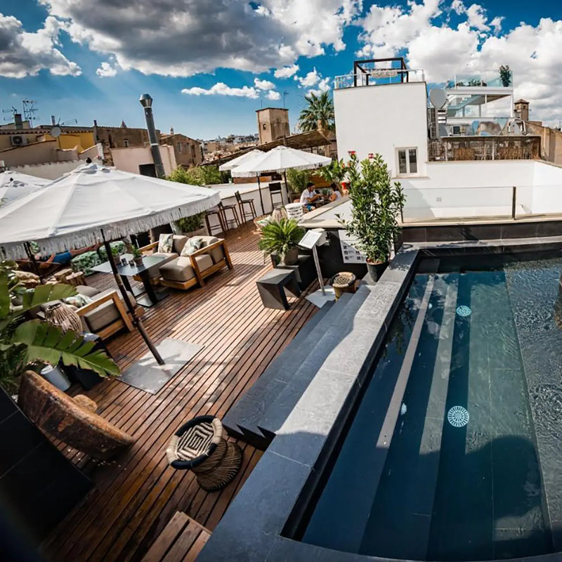 Terraza con piscina y zona lounge con sombrillas y sofás, en la azotea de un edificio en Palma de Mallorca, bajo un cielo parcialmente nublado