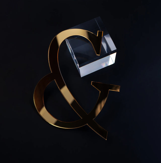 Símbolo de ampersand dorado junto a un cubo de cristal sobre fondo negro.