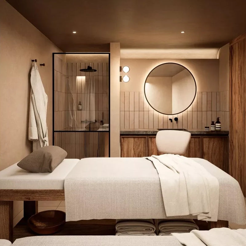 Sala de masajes del spa de Santa Ponsa, con decoración en tonos cálidos, ducha acristalada y camilla cubierta con toallas blancas.