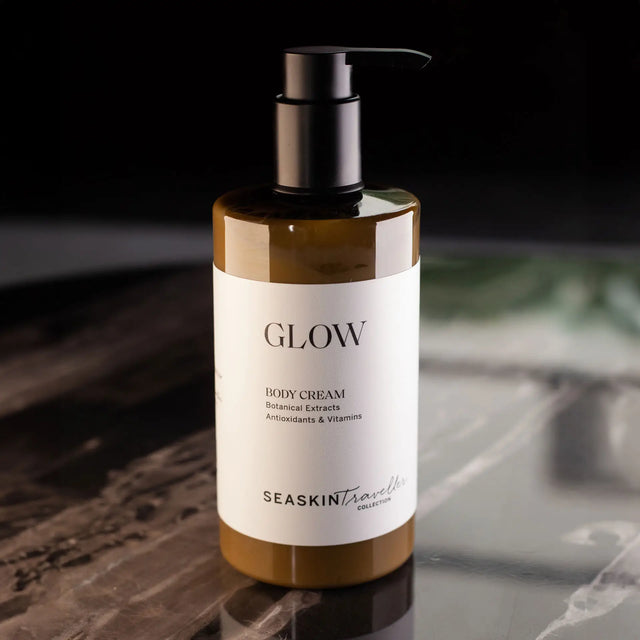 Botella con dispensador de bomba de crema corporal 'GLOW' de la colección SEASKIN Traveller, con extractos botánicos, antioxidantes y vitaminas. La crema es de color marrón claro