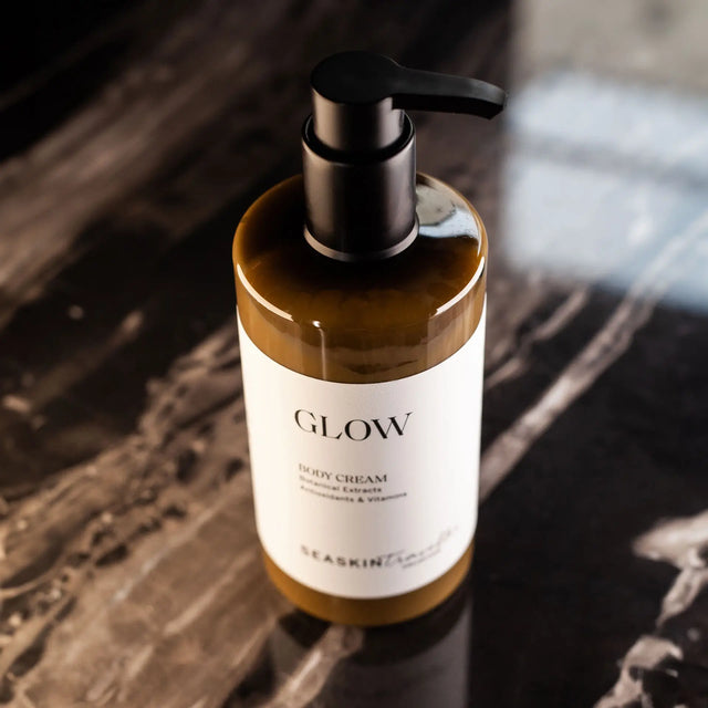 Botella con dispensador de bomba de crema corporal 'GLOW' de la colección SEASKIN Traveller, con extractos botánicos, antioxidantes y vitaminas. La crema es de color marrón claro