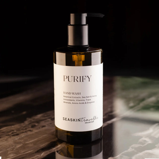 Botella ámbar con dispensador de bomba de jabón de manos 'PURIFY' de la colección SEASKIN Traveller. La etiqueta menciona que contiene extractos botánicos, sal marina, miel, antioxidantes, vitaminas, oligoelementos, aminoácidos y enzimas.