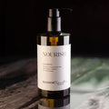 Botella ámbar con dispensador de bomba de champú 'NOURISH' de la colección SEASKIN Traveller. La etiqueta blanca detalla extractos botánicos, sal marina, antioxidantes, vitaminas y oligoelementos.