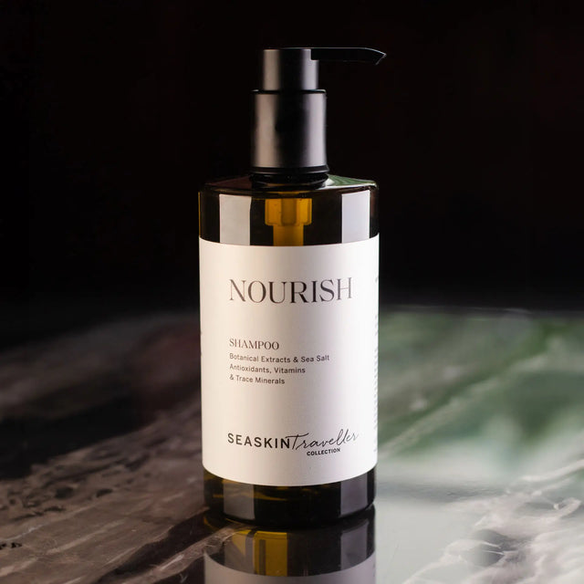 Botella ámbar con dispensador de bomba de champú 'NOURISH' de la colección SEASKIN Traveller. La etiqueta blanca detalla extractos botánicos, sal marina, antioxidantes, vitaminas y oligoelementos.