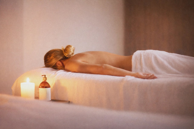 Mujer recibiendo un masaje relajante en un spa, acostada sobre una camilla con una vela encendida y un frasco de aceite al lado.